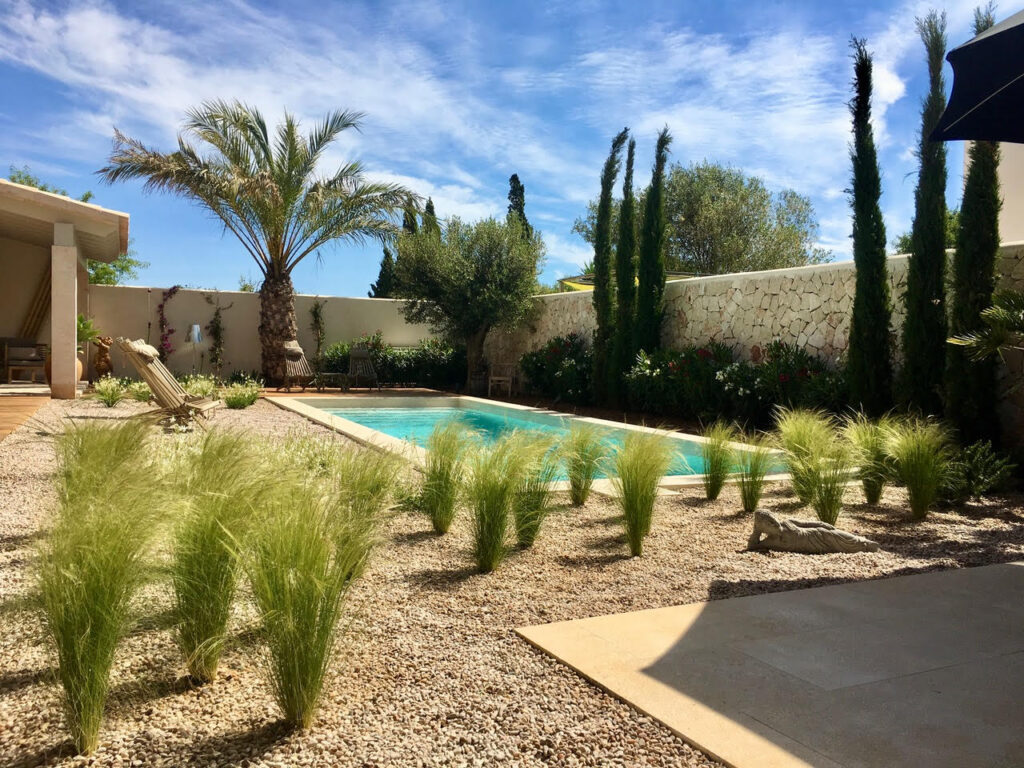 Villengarten auf Mallorca mit Pool, Zypressen und Ziergräsern in Kiesflächen — ohne Rasen