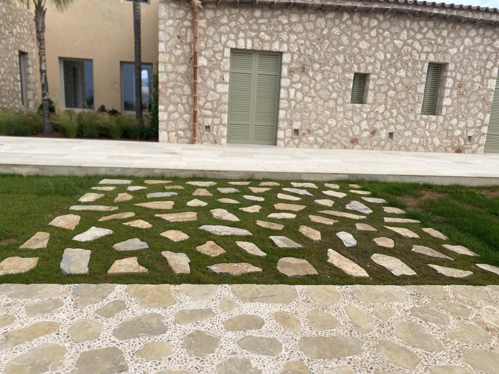 Stone slabs set into lawn and continuous stone paving in front of a Mallorcan country house